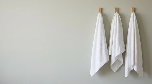Tres toallas blancas de hostelería colgadas en ganchos de madera: dónde comprarlas sin pedido mínimo